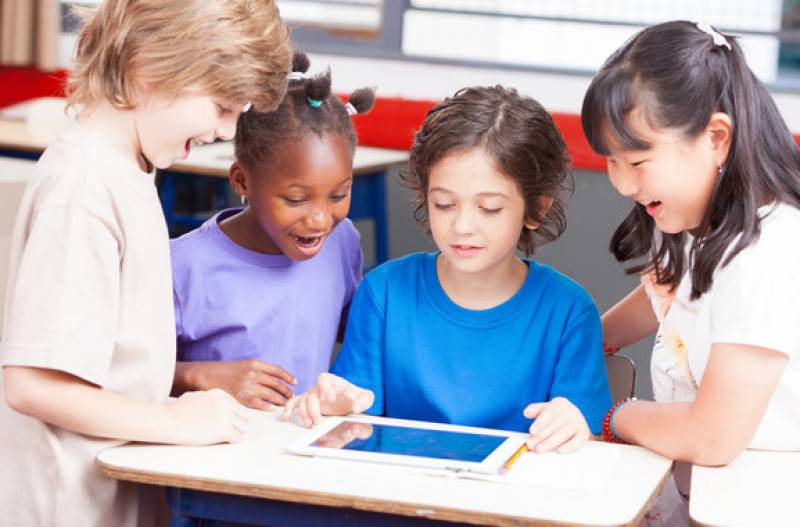 Niños de diversas etnias hablando alrededor de una tableta. / Fotolia