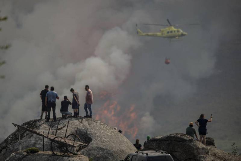 Varias personas observan la labor de un helicóptero de extinción de un incendio