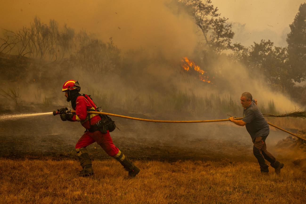 Un efectivo de la Unidad Militar de Emergencias (UME) y un vecino de la localidad de A Espasa trabajan durante el incendio forestal que permanece activo en Chandrexa de Queixa (Ourense), este martes. / EFE | Brais Lorenzo