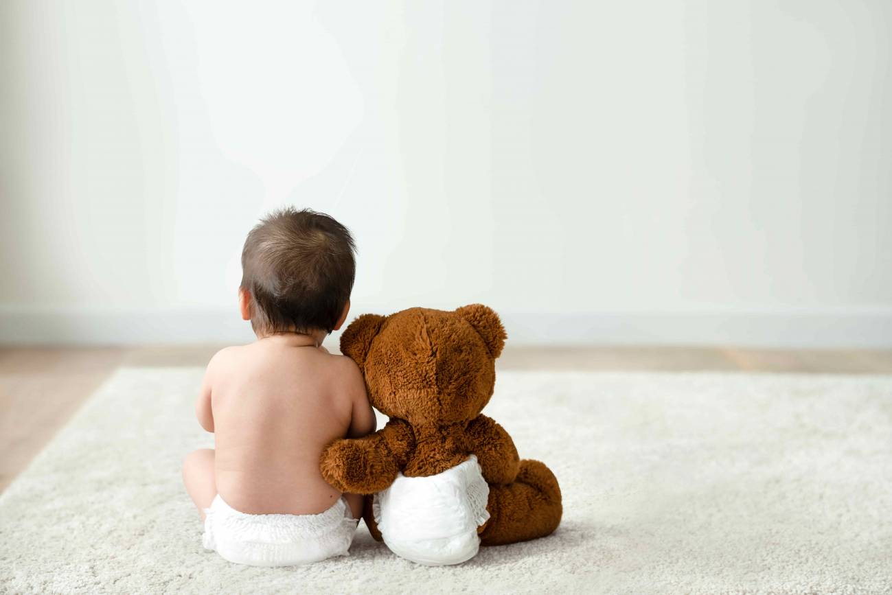 bebe con un oso de peluche de espaldas