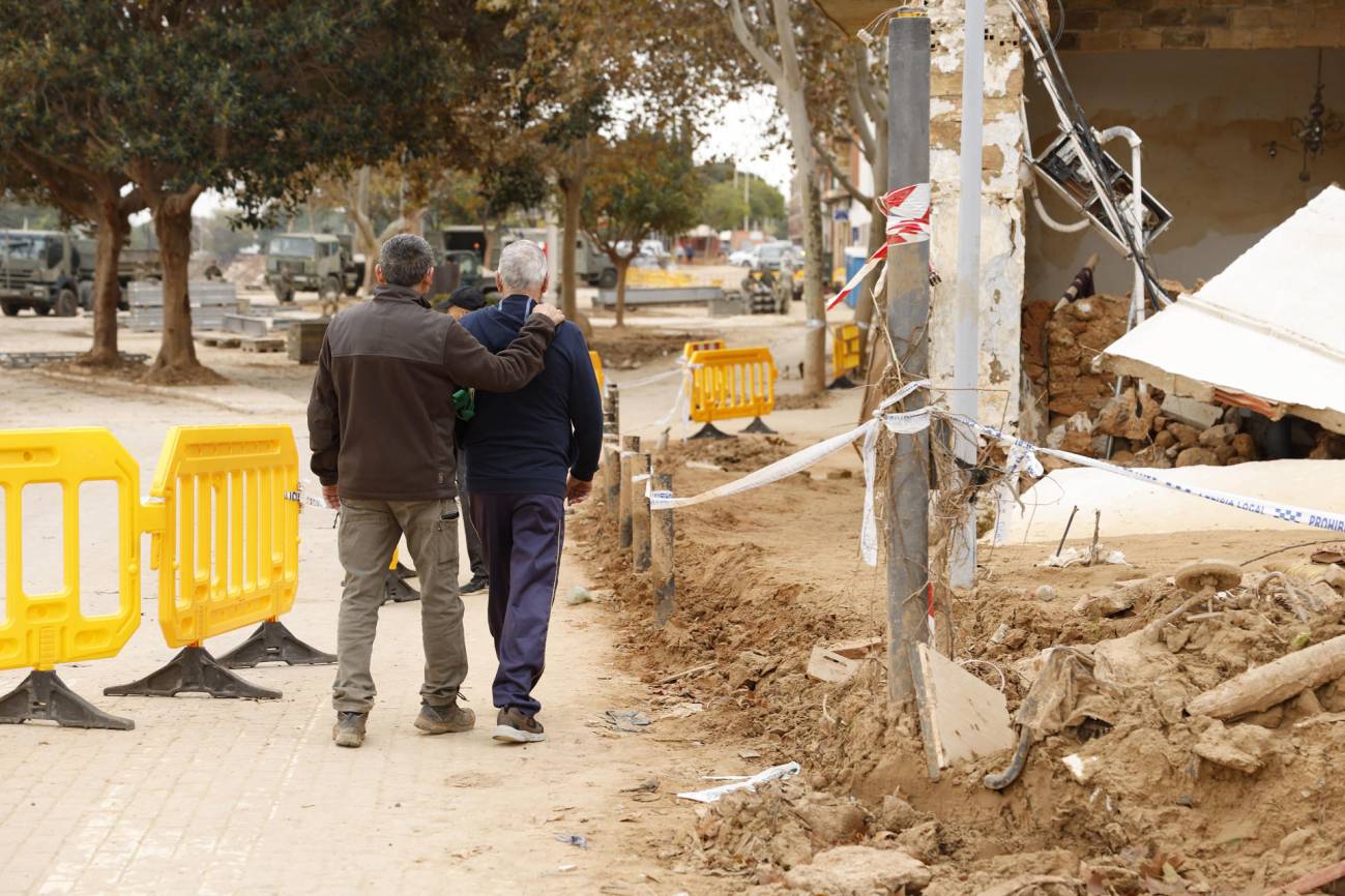 Dos personas caminan junto a una vivienda destrozada por el paso de la DANA