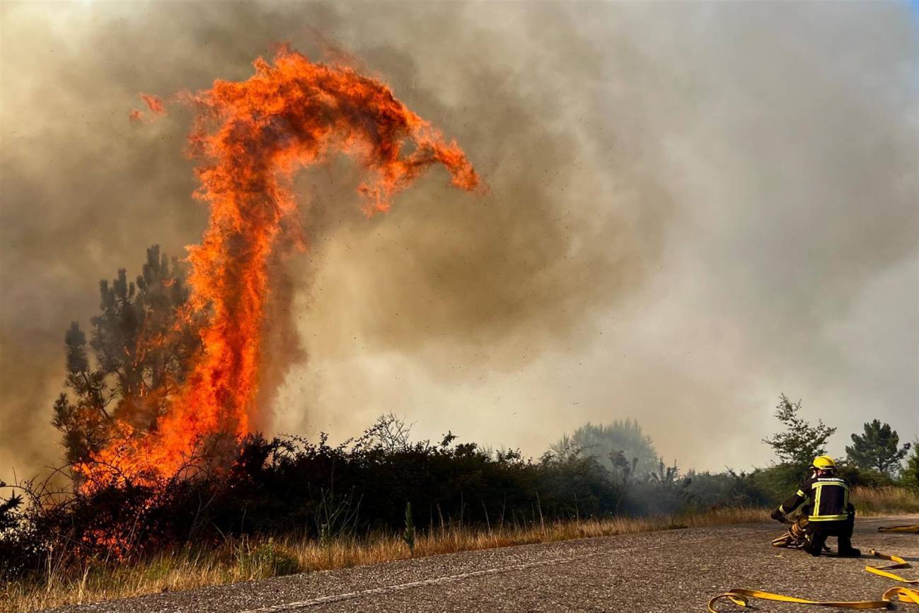 Efectivos de bomberos en la extinción de un incendio forestal en la carretera N120 en A Cañiza (Pontevedra) . / EFE/ Alberto Sxenick