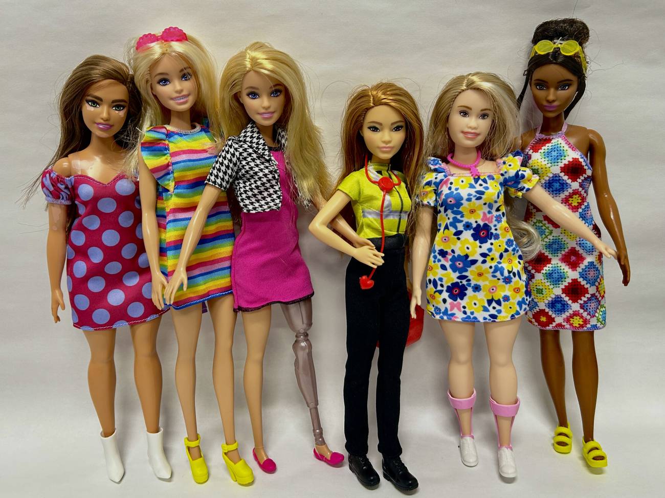 Varias barbies de distintas etnias, algunas muestran discapacidad, con tacones y zapatos planos.