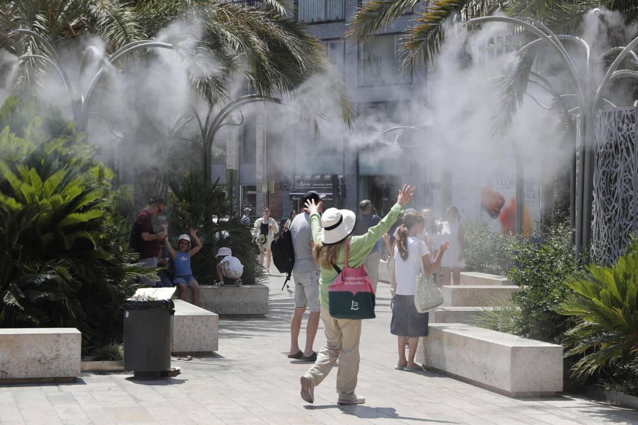En la imagen de archivo varios turistas tratan de mitigar el calor bajo una nube de agua vaporizada