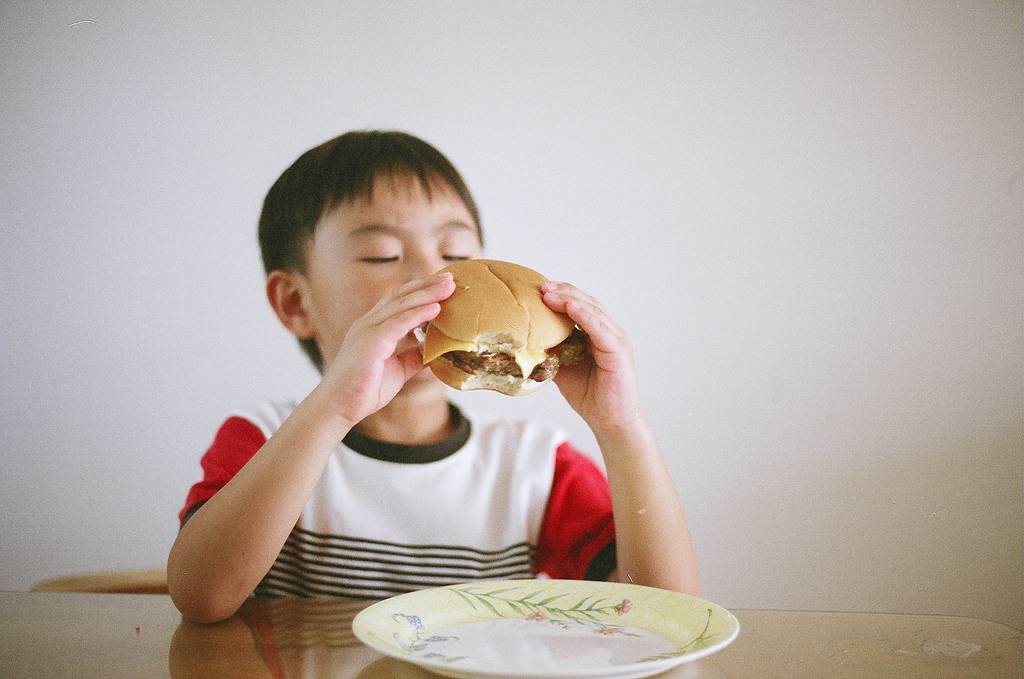 Niño comiendo una hamburguesa, alimento típico en la dieta americana