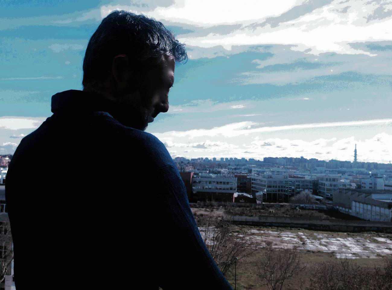 Fotomontaje titulado "La soledad". La autora es Laura Rico. Se ve de fondo un paisaje urbano frío y azulado. Y en primer término, de espaldas, la silueta a contraluz de un hombre que mira al suelo con aspecto triste. 