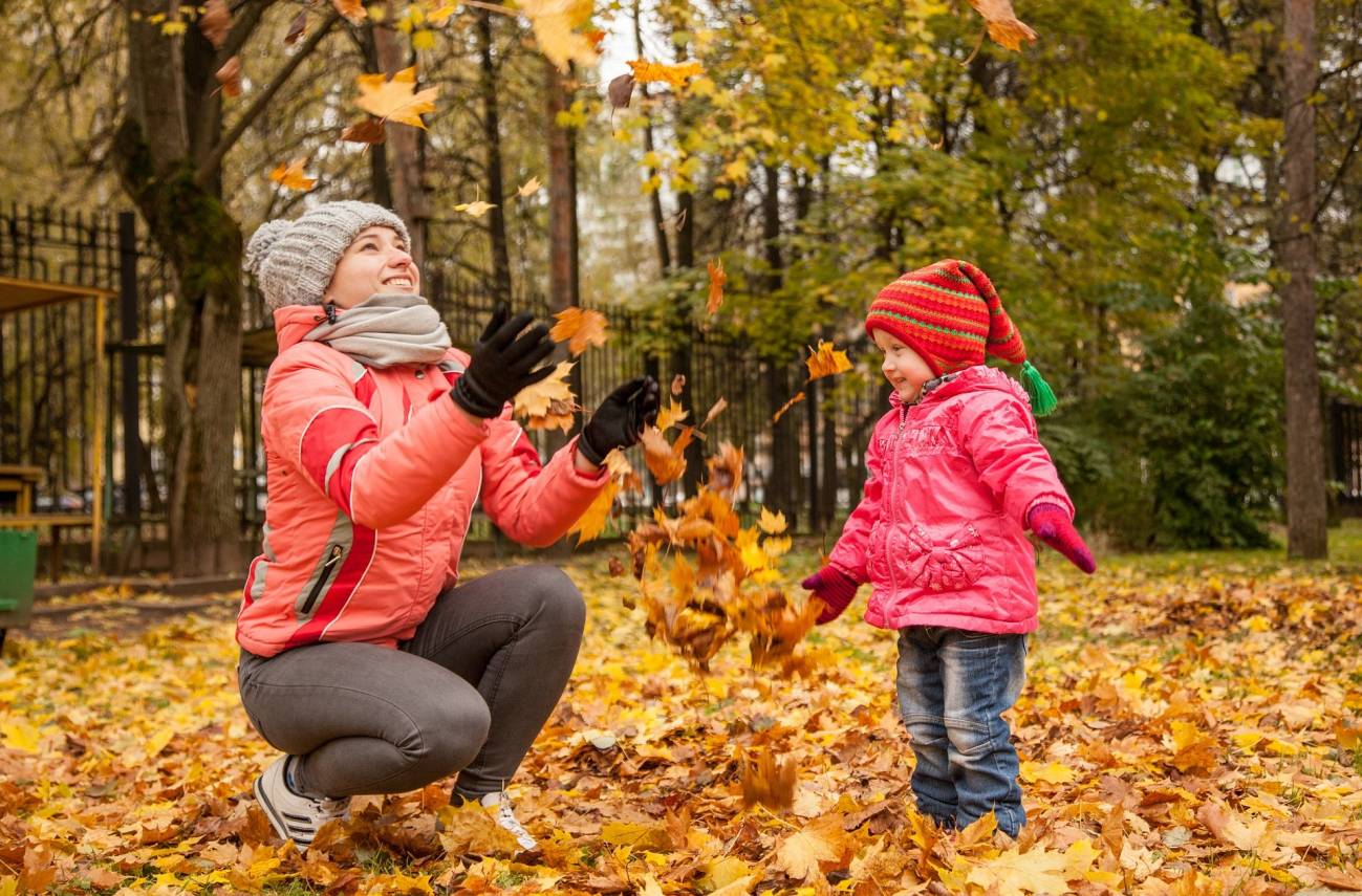 Fotografía otoñal de una mujer y un niño, jugando con las hojas caídas de  los árboles, en un parque. 