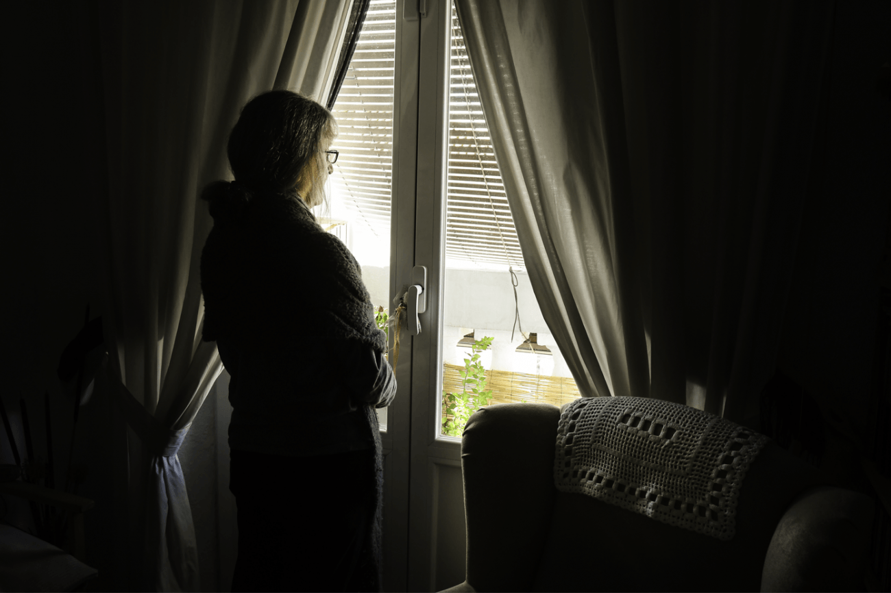Mujer adulta, confinada por la pandemia, mira hacia la calle a través de la ventana de su casa