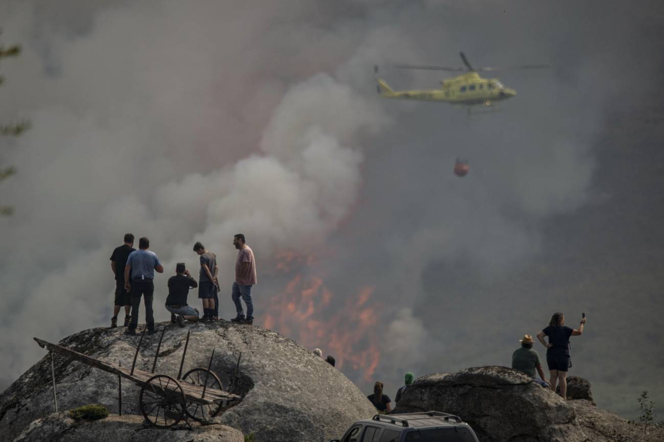 Varias personas observan la labor de un helicóptero de extinción de un incendio