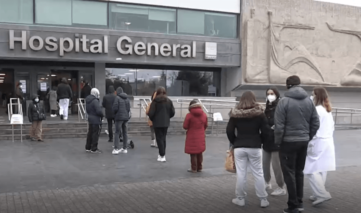 Personas con mascarillas hacen cola en la puerta de un hospital