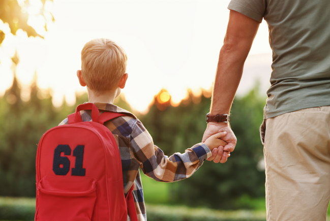 niño con mochila de espaldas y con su padre de la mano 