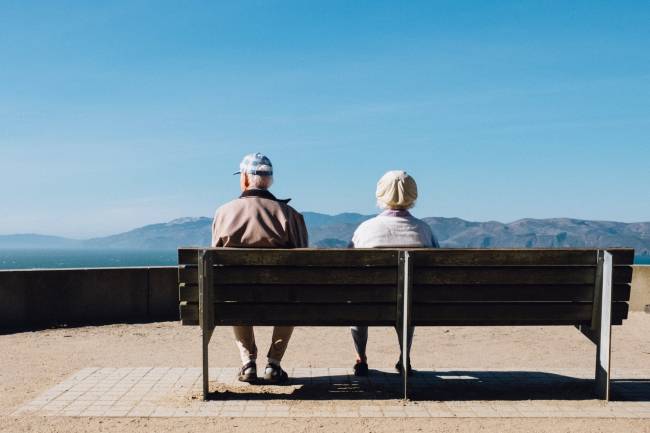 Dos ancianos sentados en un banco mirando hacia el horizonte costero