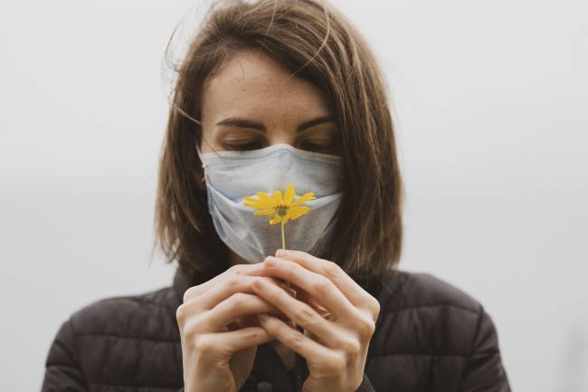 Mujer con mascarilla oliendo una flor