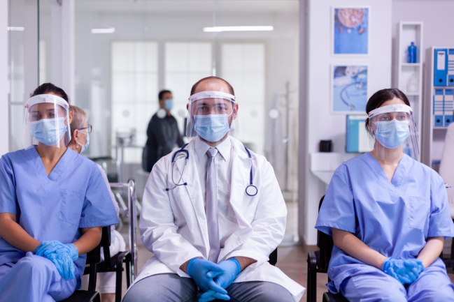 dos enfermeras y un médico sentados y con el equipo de protección