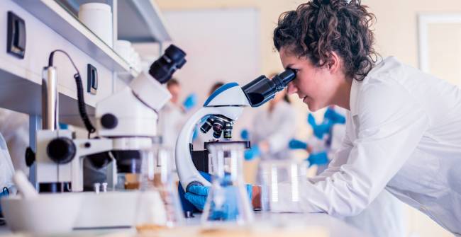 Científica mira a través de microscopio en un laboratorio