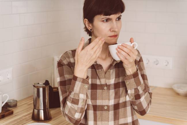 Mujer huele el café con una expresión desconcertada