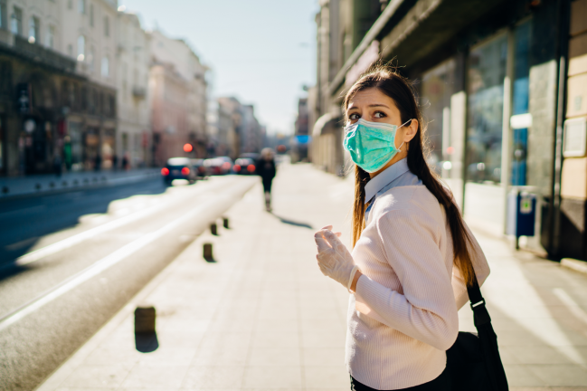 mujer con mascarilla en la calle mira hacia atrás con ansiedad