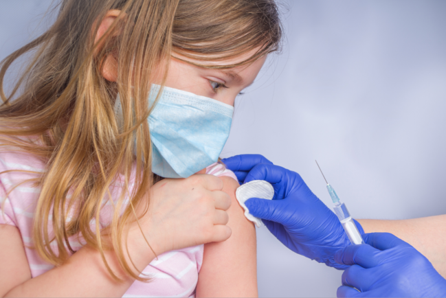 niña con mascarilla a la que le ponen una vacuna