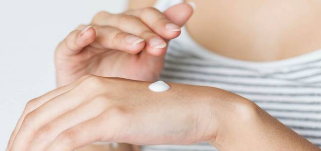 mujer echando crema en sus manos