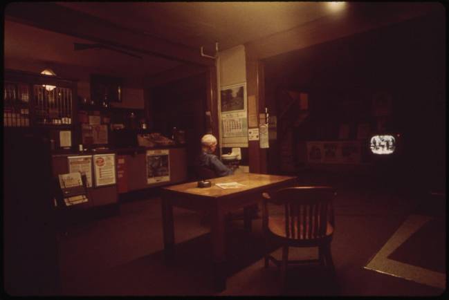 Fotografía en penumbra de una persona mayor viendo la televisión en un bar.