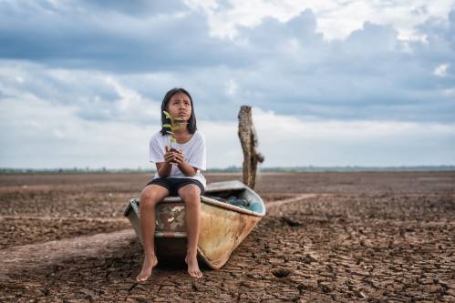 Niña asiática sostiene una planta en medio de un paisaje árido