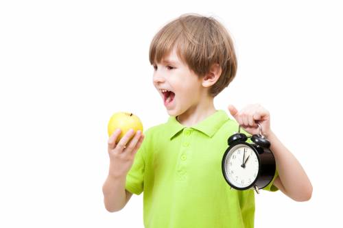Un niño sujetando una manzana y un reloj. 