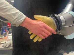 Mano humana estrecha mano de un robot con piel artificial que tiene tacto